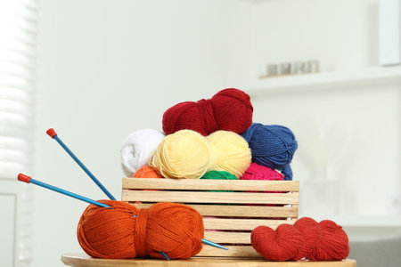 Skeins of soft yarn in crate and knitting needles on wooden table indoorsの写真素材