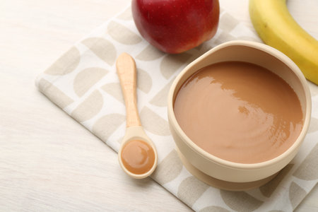 Delicious baby food in bowl and ingredients on white wooden tableの写真素材
