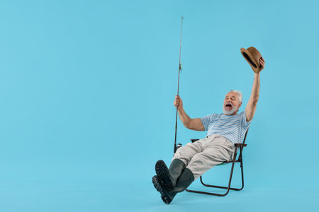 Fisherman with rod on fishing chair against light blue background. Space for textの写真素材