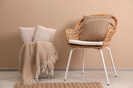 Soft pillows, wicker chair and blanket on floor near beige wallの写真素材