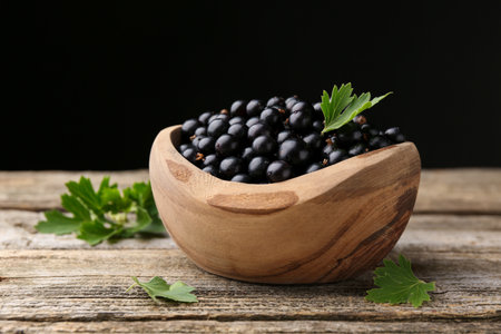 Ripe black currants and leaves in bowl on wooden tableの写真素材