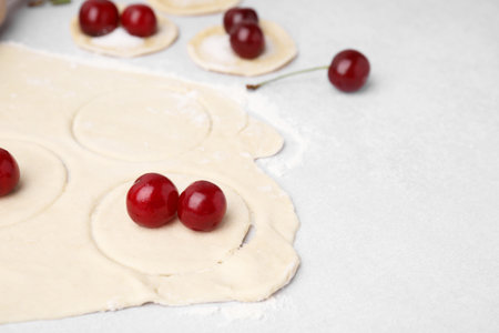 Process of making dumplings (varenyky) with cherries. Raw dough and ingredients on light table, closeup. Space for textの写真素材