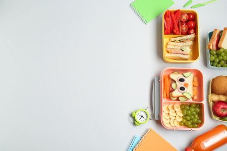 Lunch boxes with snacks, alarm clock and stationery on white background, flat lay. Space for textの写真素材