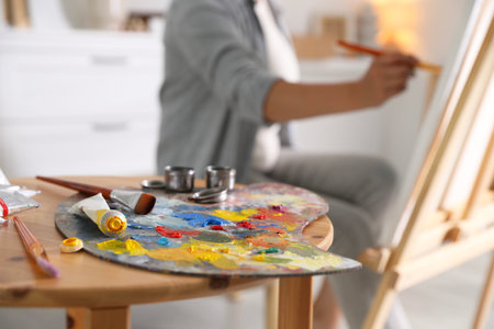 Woman painting on easel indoors, focus on palette and brushesの写真素材