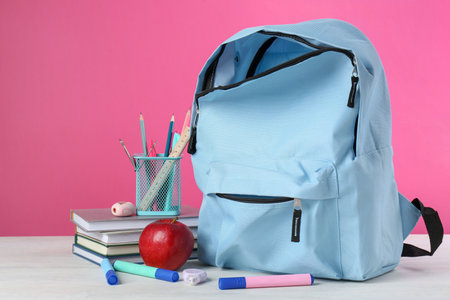 Backpack with different school stationery and apple on light table against pink backgroundの写真素材