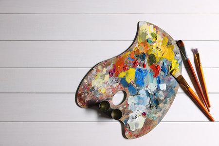 Artist's palette, brushes, paints on white wooden table, flat lay. Space for textの写真素材