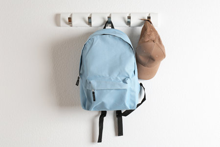 Light blue backpack and cap hanging on white wallの写真素材