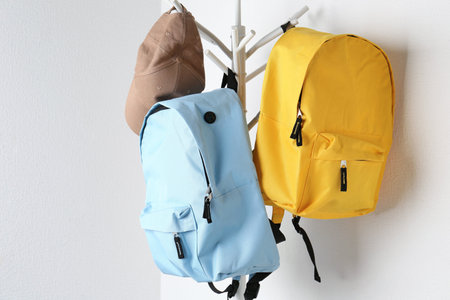 Bright backpacks and cap hanging on white wall