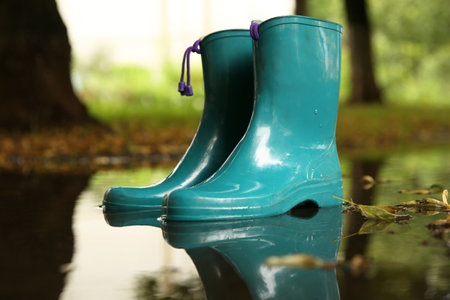 Pair of colorful rubber boots in puddle outdoors