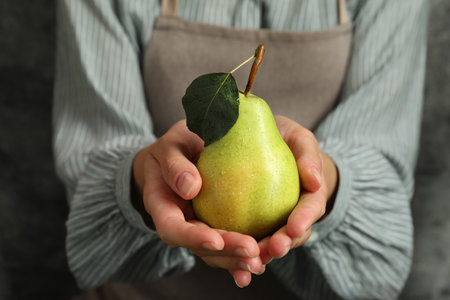 Woman with ripe pear near grey wall, closeupの写真素材
