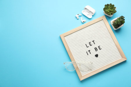 Letter board with phrase Let It Be, glasses, houseplants and earphones on light blue background,...