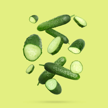 Many ripe cucumbers falling on yellowish green backgroundの写真素材