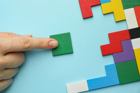 Woman playing with colorful wooden puzzle pieces on light blue background, top view