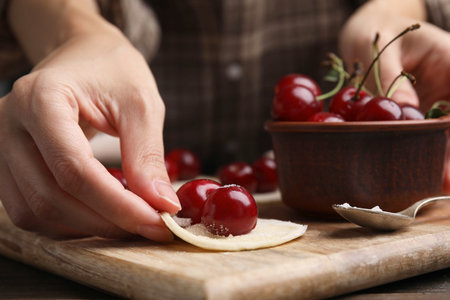 Woman making dumplings (varenyky) with cherries at wooden table, closeupの写真素材