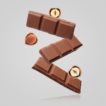 Pieces of tasty chocolate and hazelnuts falling on light grey backgroundの写真素材