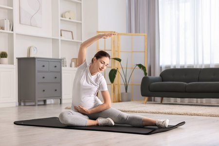 Beautiful pregnant woman doing stretching exercises on mat at homeの写真素材