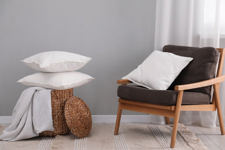 Stack of white pillows, armchair and wicker basket on floor indoorsの写真素材