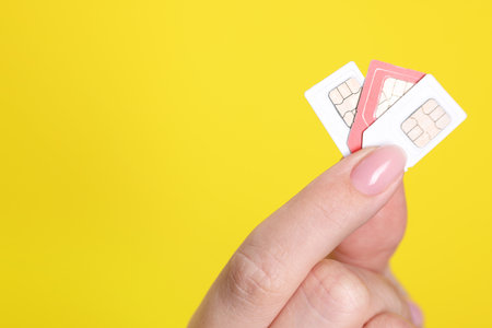 Woman holding SIM cards on yellow background, closeup. Space for textの写真素材