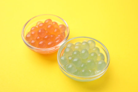 Bright tapioca pearls in bowls on yellow background, closeup