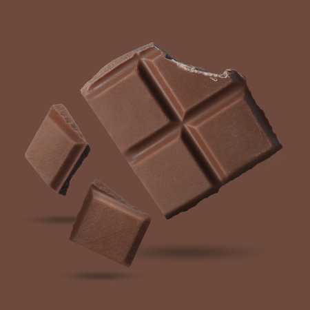 Pieces of sweet chocolate falling on brown background