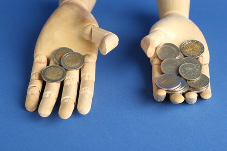 Financial inequality. Uneven amount of coins in mannequin hands on blue background