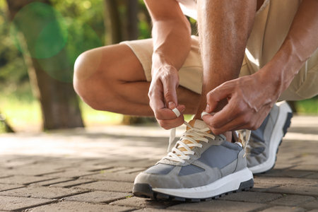 Man tying shoelace of grey sneaker outdoors, closeupの写真素材