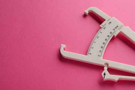 Plastic body fat caliper on pink background, closeup. Space for textの写真素材