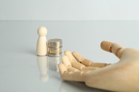 Financial inequality. Human figure, coins and wooden hand on light tableの写真素材