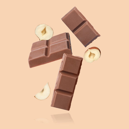 Pieces of tasty chocolate and hazelnuts falling on dark beige backgroundの写真素材