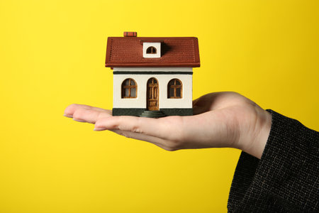 Woman with house model on yellow background, closeupの写真素材