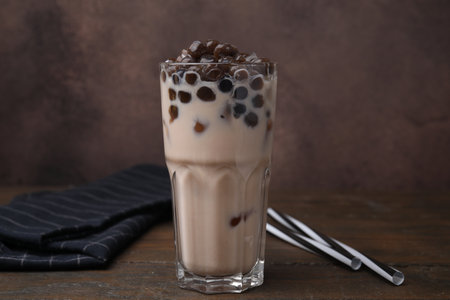 Tasty milk bubble tea in glass on wooden table against brown backgroundの写真素材