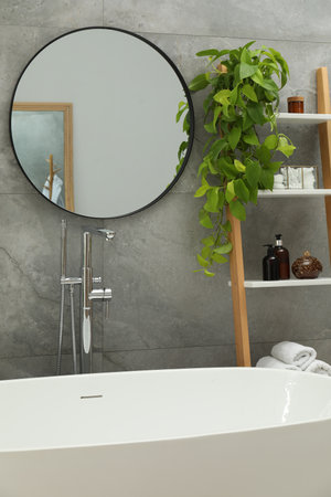 Round mirror on grey tiled wall over tub in bathroom