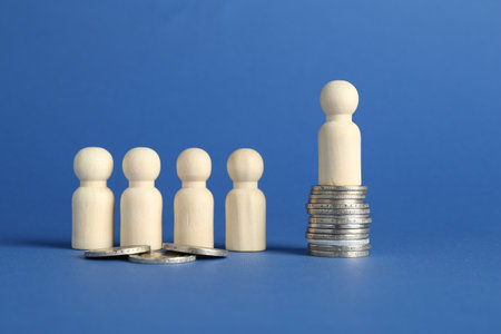 Financial inequality. Wooden figures with uneven amount of coins on blue background