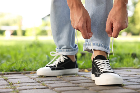 Man tying shoelace of black sneaker outdoors, closeup. Space for text