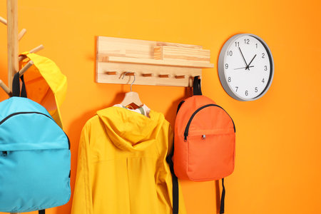 Bright backpacks, cap, coat and clock near orange wallの写真素材