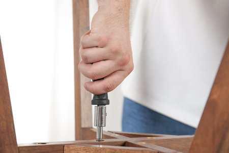 Man with screwdriver assembling furniture indoors, closeupの写真素材