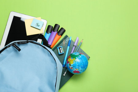 Light blue school backpack with stationery on green background, top view. Space for text