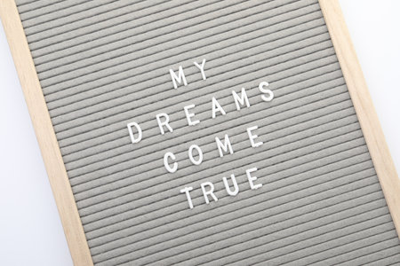 Letter board with phrase My dreams come true on white background, top view