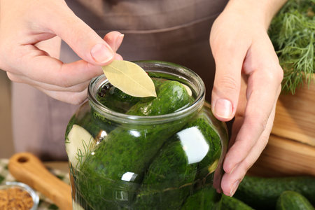 Making pickles. Woman putting bay leaf into glass jar at table, closeupの写真素材
