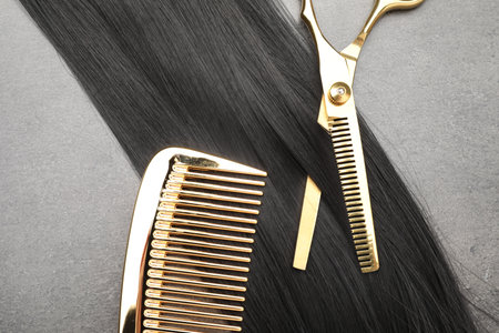 Black hair strand, comb and professional scissors on gray surface, flat layの写真素材