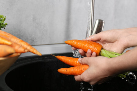 Woman washing fresh carrots under tap water in above sink indoors, closeupの写真素材