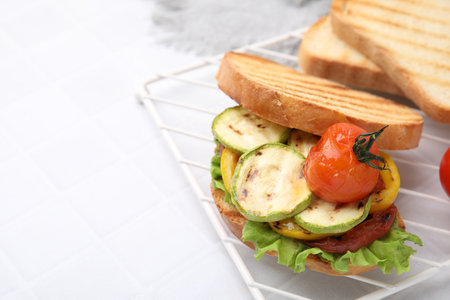 Tasty sandwich with grilled vegetables on white tiled table, closeup. Space for textの写真素材
