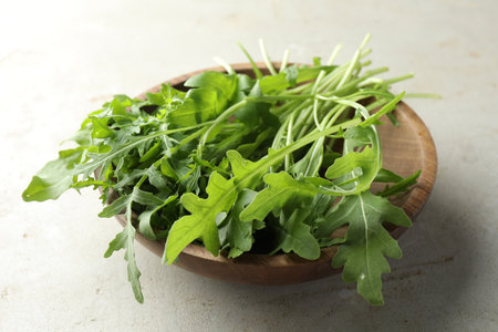 Many fresh arugula leaves in bowl on gray textured table, closeup