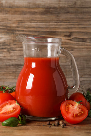 Tasty tomato juice in glass jug, fresh vegetables and spices on wooden tableの写真素材