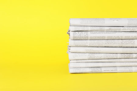 Stack of newspapers in different languages on yellow background, space for textの写真素材