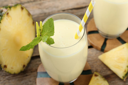 Tasty pineapple smoothie in glass, mint and slices of fruit on wooden table, closeupの写真素材