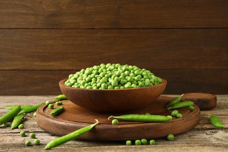 Fresh green peas in bowl and pods on wooden tableの写真素材