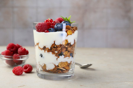 Tasty yogurt with fresh berries, granola and mint in glass on gray textured table, space for text