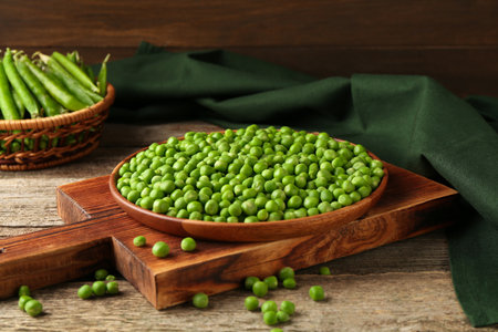 Fresh green peas in bowl and pods on wooden tableの写真素材