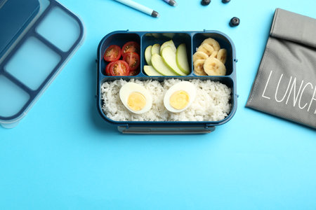 Bag and lunch box with snacks on light blue background, flat lay. Space for textの写真素材
